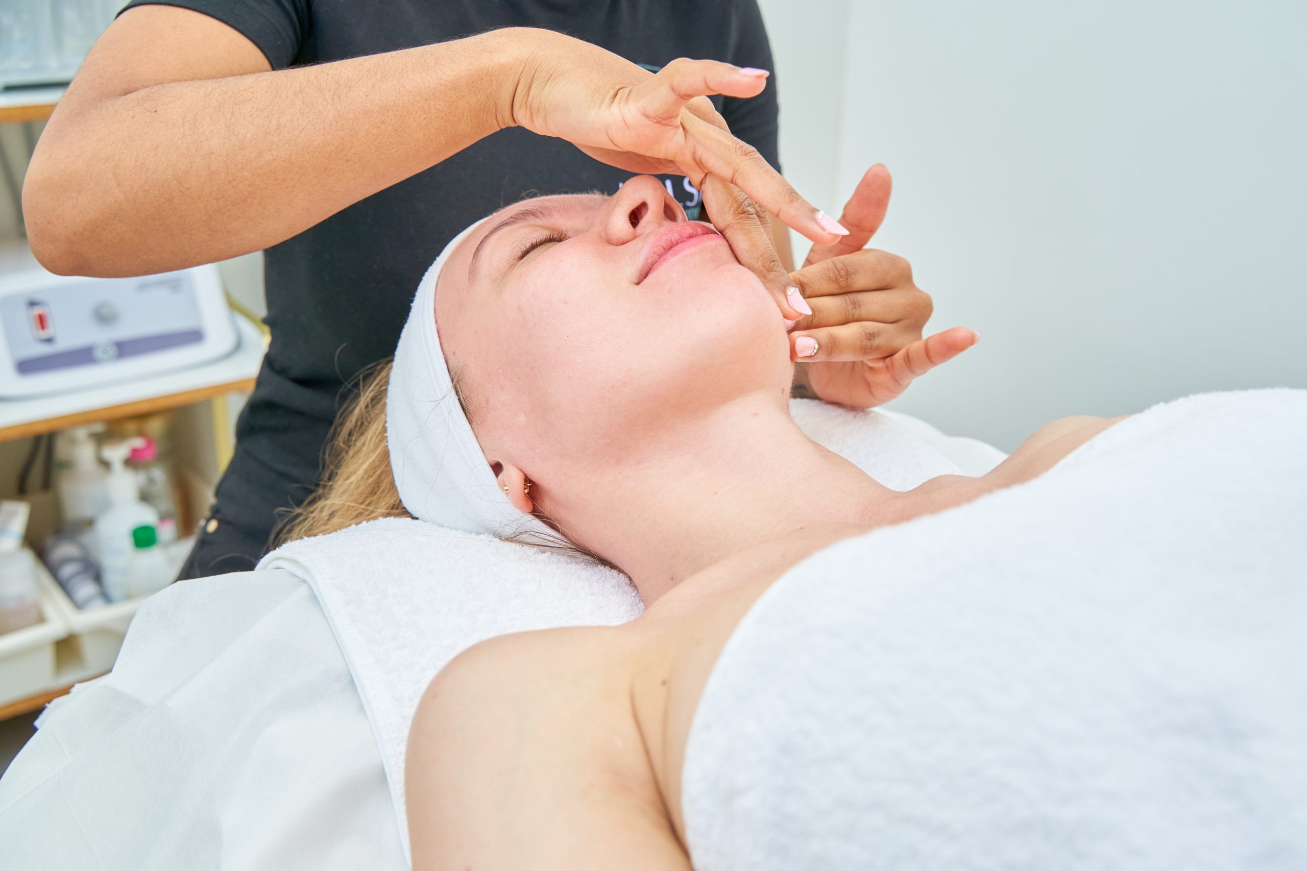 a beauty salon worker performs a facial treatment on a client by massaging her face with creams with her hands.
